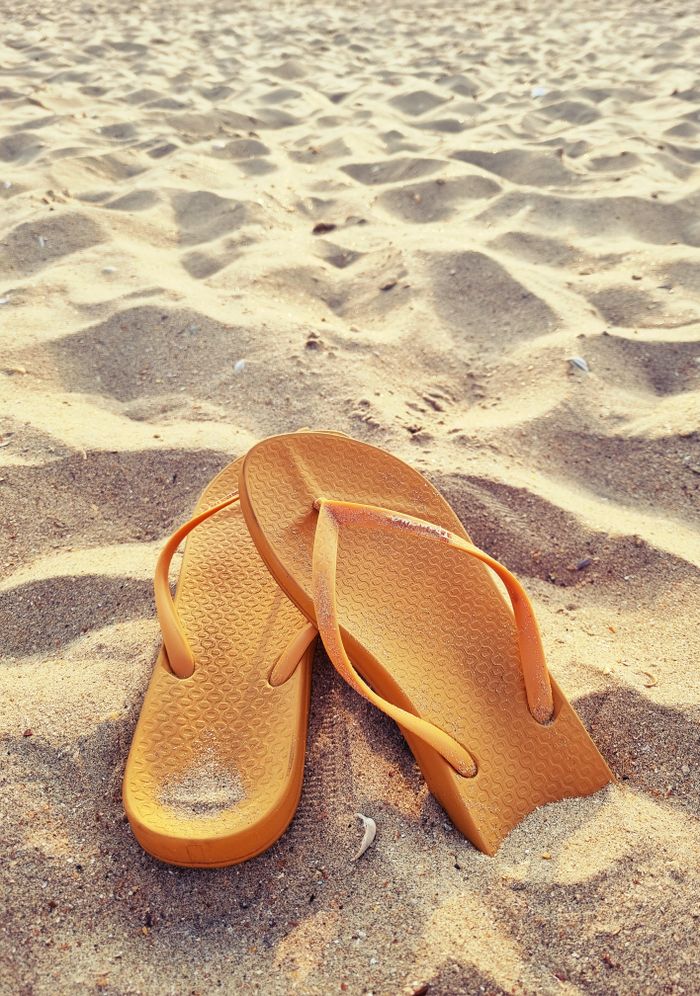 A pair of yellow flip flops on a sandy beach, capturing a sunny summer vibe.