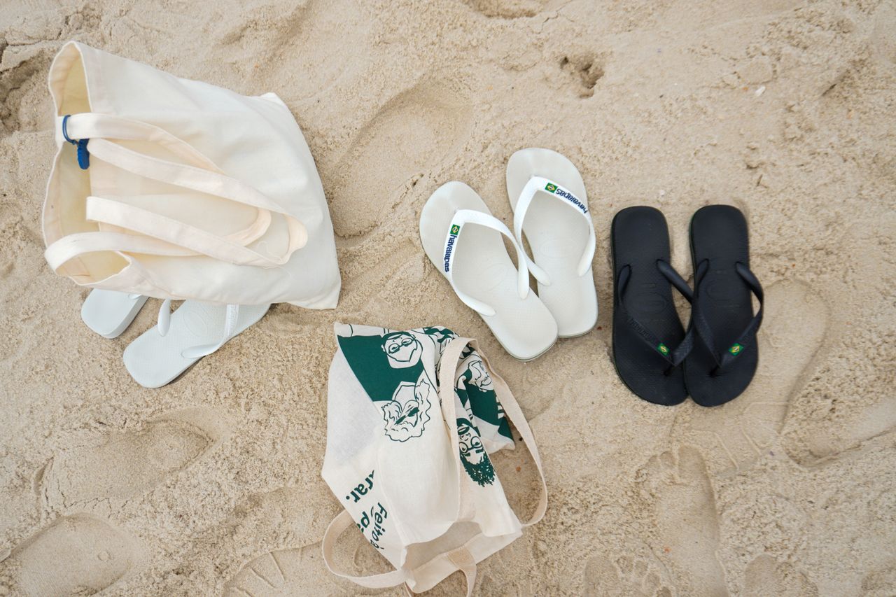 Flat lay of sandals and a tote bag on a sandy beach, ideal for summer themes.