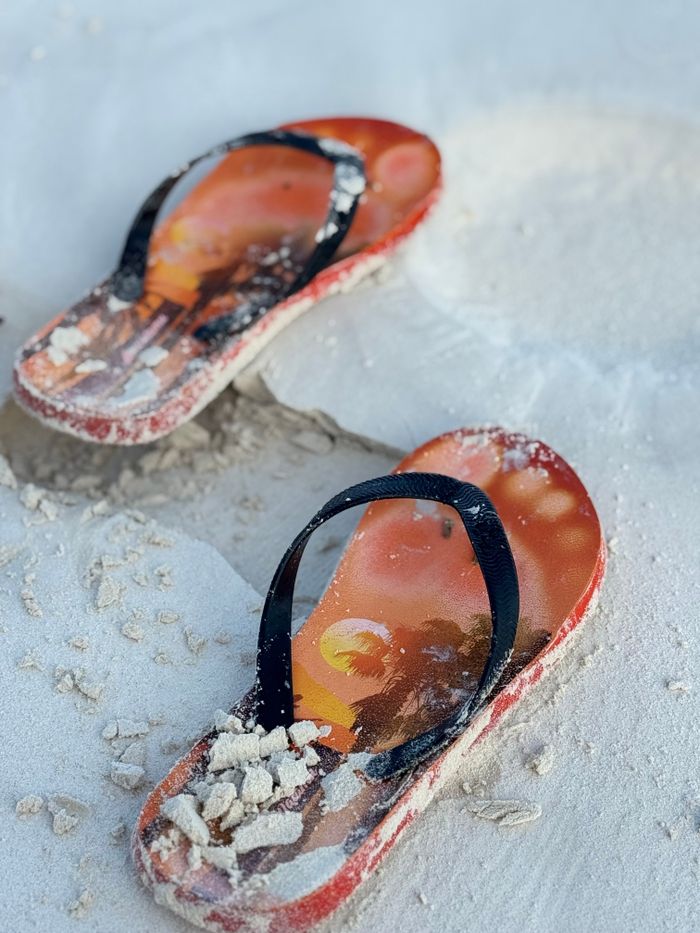 Pair of flip-flops on sandy beach, perfect for summer vacation imagery.