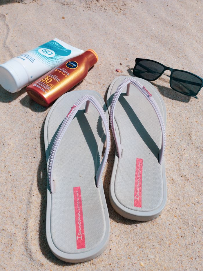 Flip-flops, sunscreen, and sunglasses on sandy beach, perfect for summer vacations.