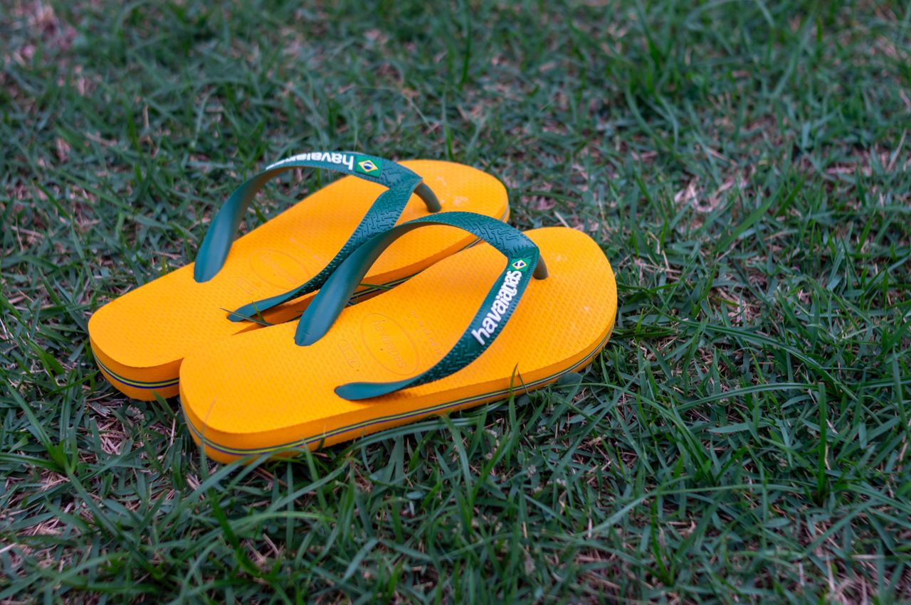Bright yellow flip flops with green straps resting on lush green grass, creating a summery feel.